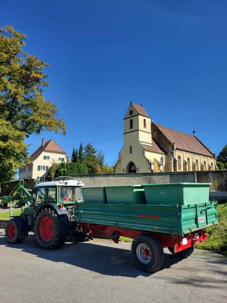 Traktor mit Bottichen bei der Weinlese vor der Kirche in Bamlach
